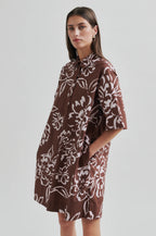 Woman wearing a brown floral patterned dress on a plain background