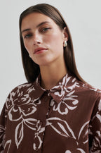 Woman wearing a brown floral patterned shirt against a plain background