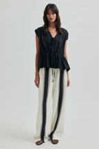 Woman wearing a black top and white pants with black stripes on a white background