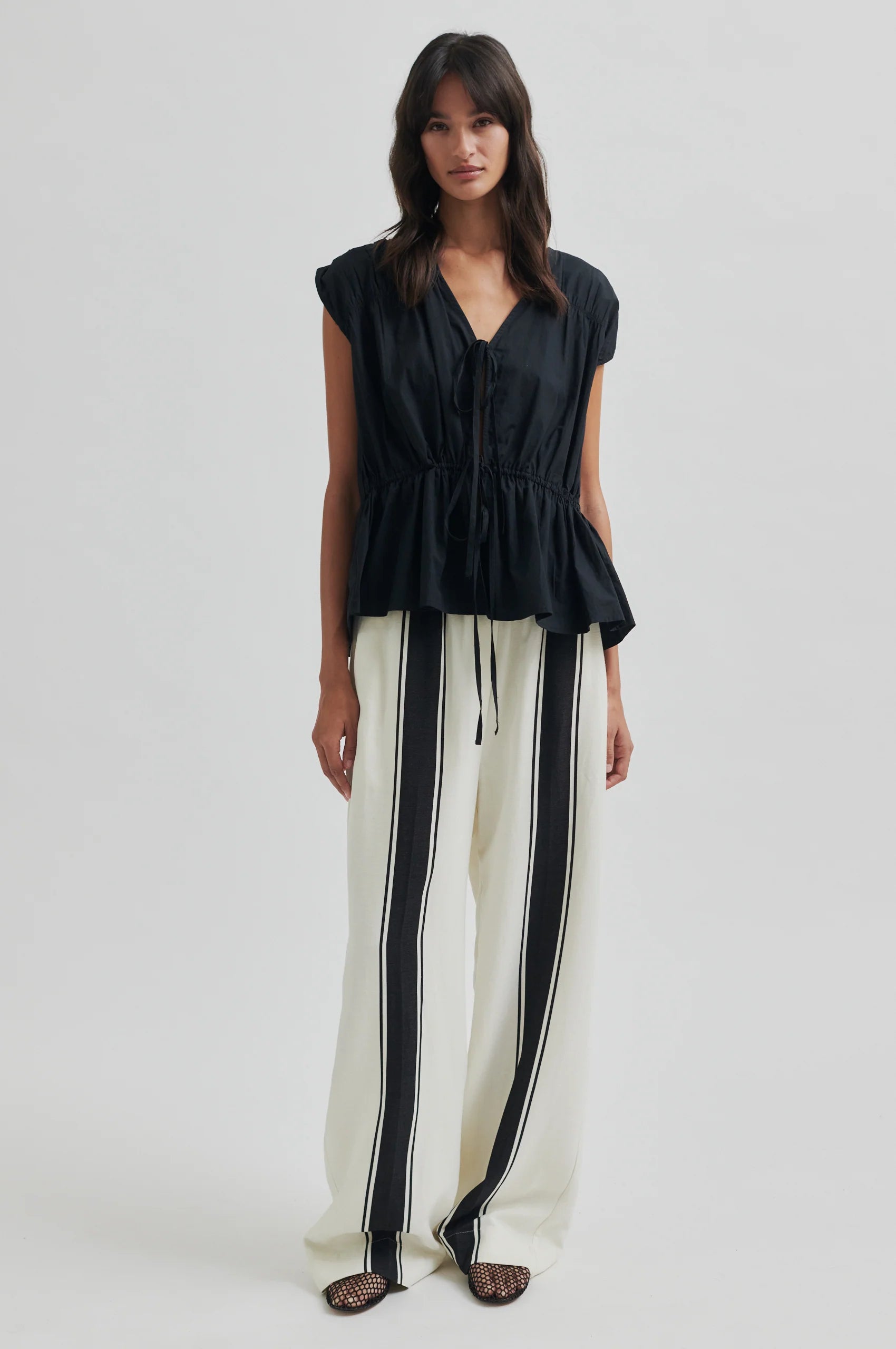 Woman wearing a black top and white pants with black stripes on a white background
