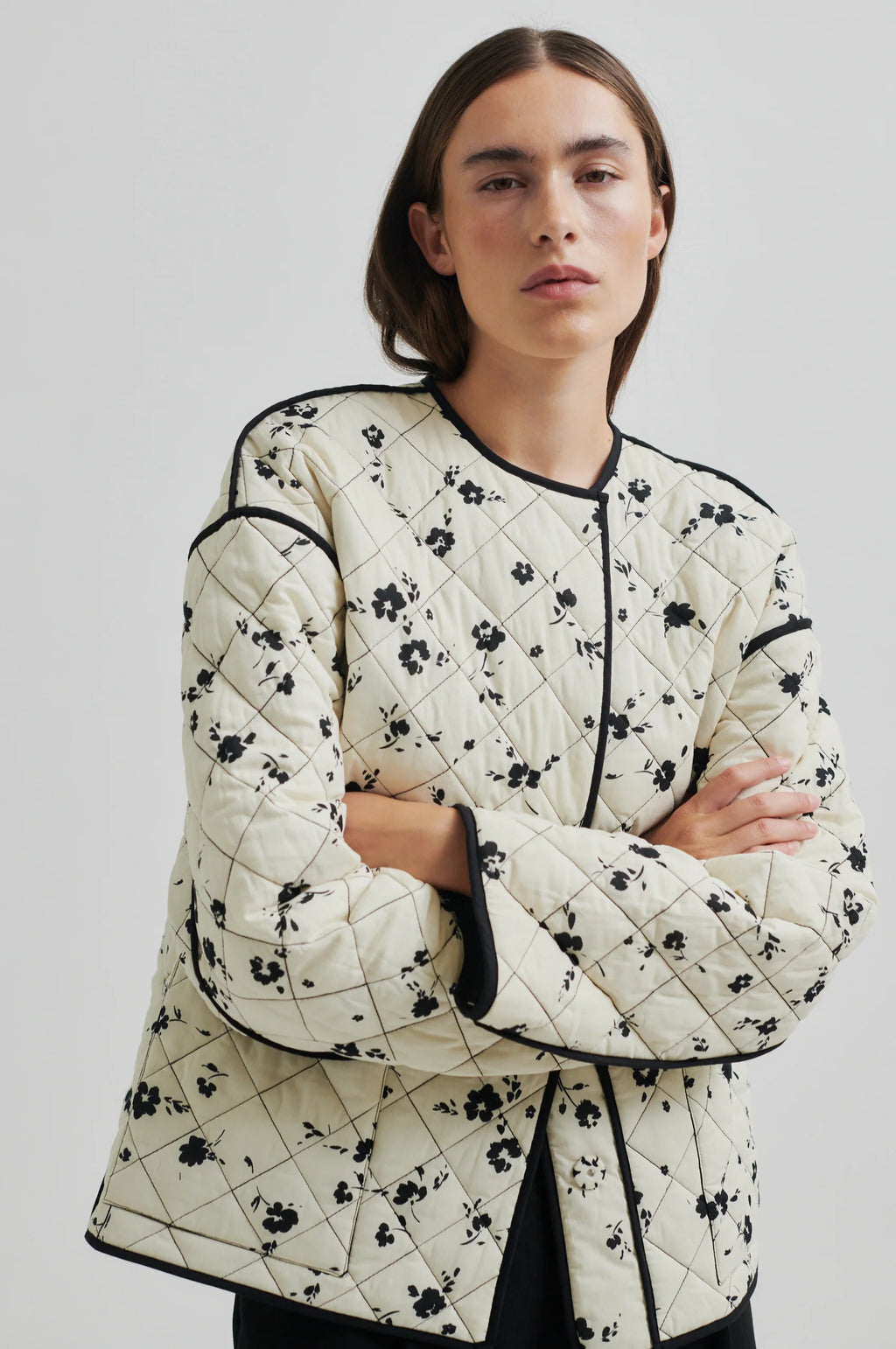 Person wearing a quilted jacket with black floral patterns on a plain background