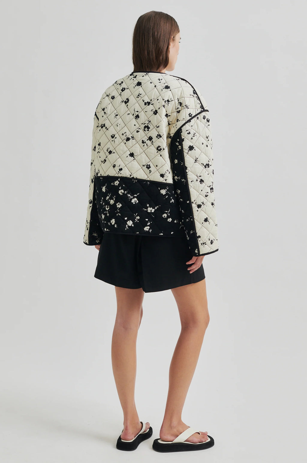 Person wearing a black and white floral quilted jacket on a plain background