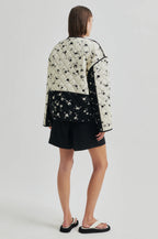 Person wearing a black and white floral quilted jacket on a plain background