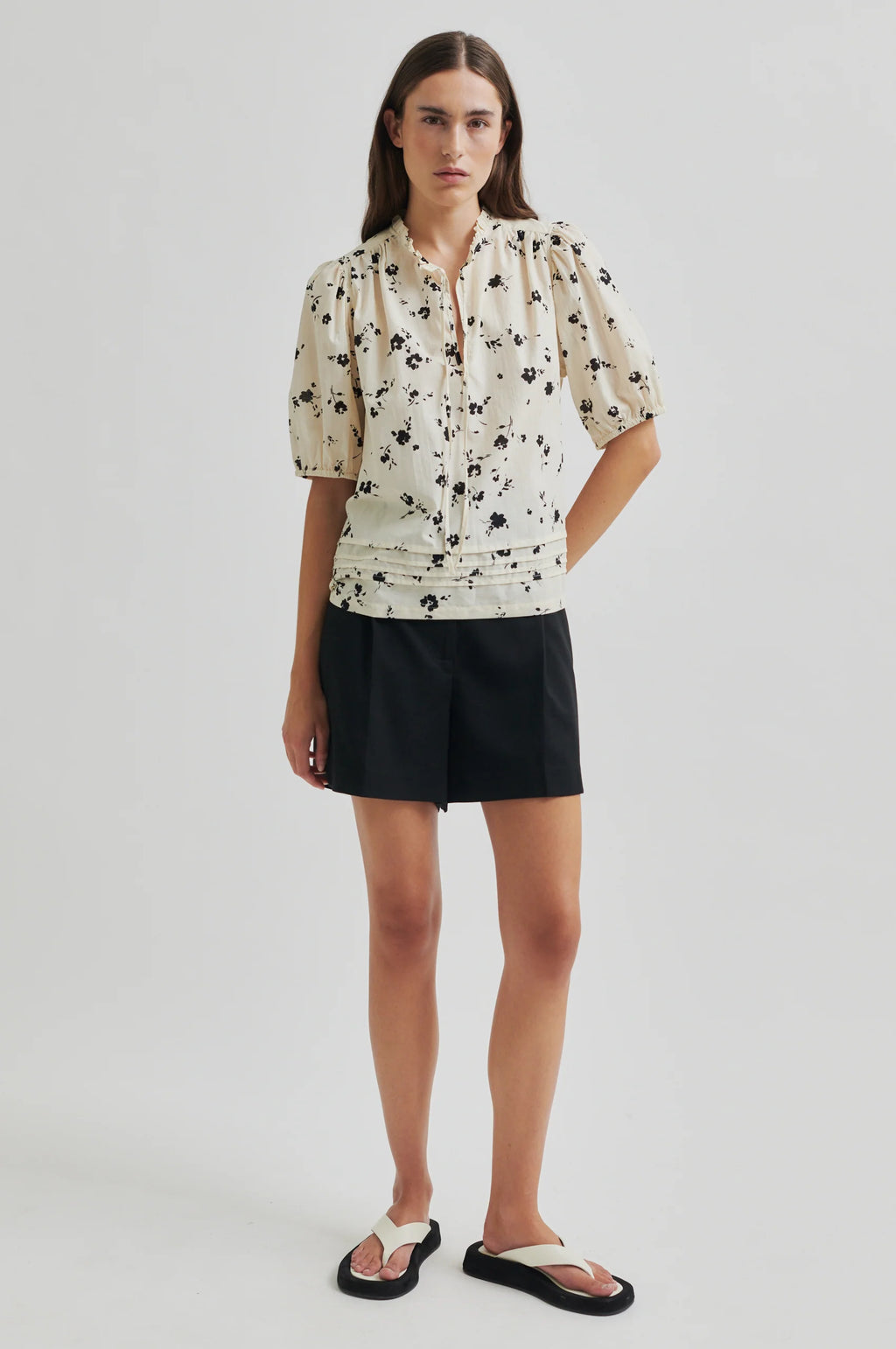 Woman wearing a floral blouse and black shorts on a plain background