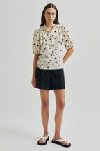 Woman wearing a floral blouse and black shorts on a plain background