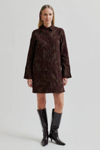 Woman wearing a brown textured outfit with black boots on a light gray background