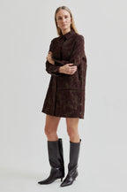 Woman wearing a brown patterned dress with black knee-high boots on a light gray background