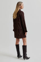 Woman wearing a brown textured outfit with black knee-high boots on a light gray background