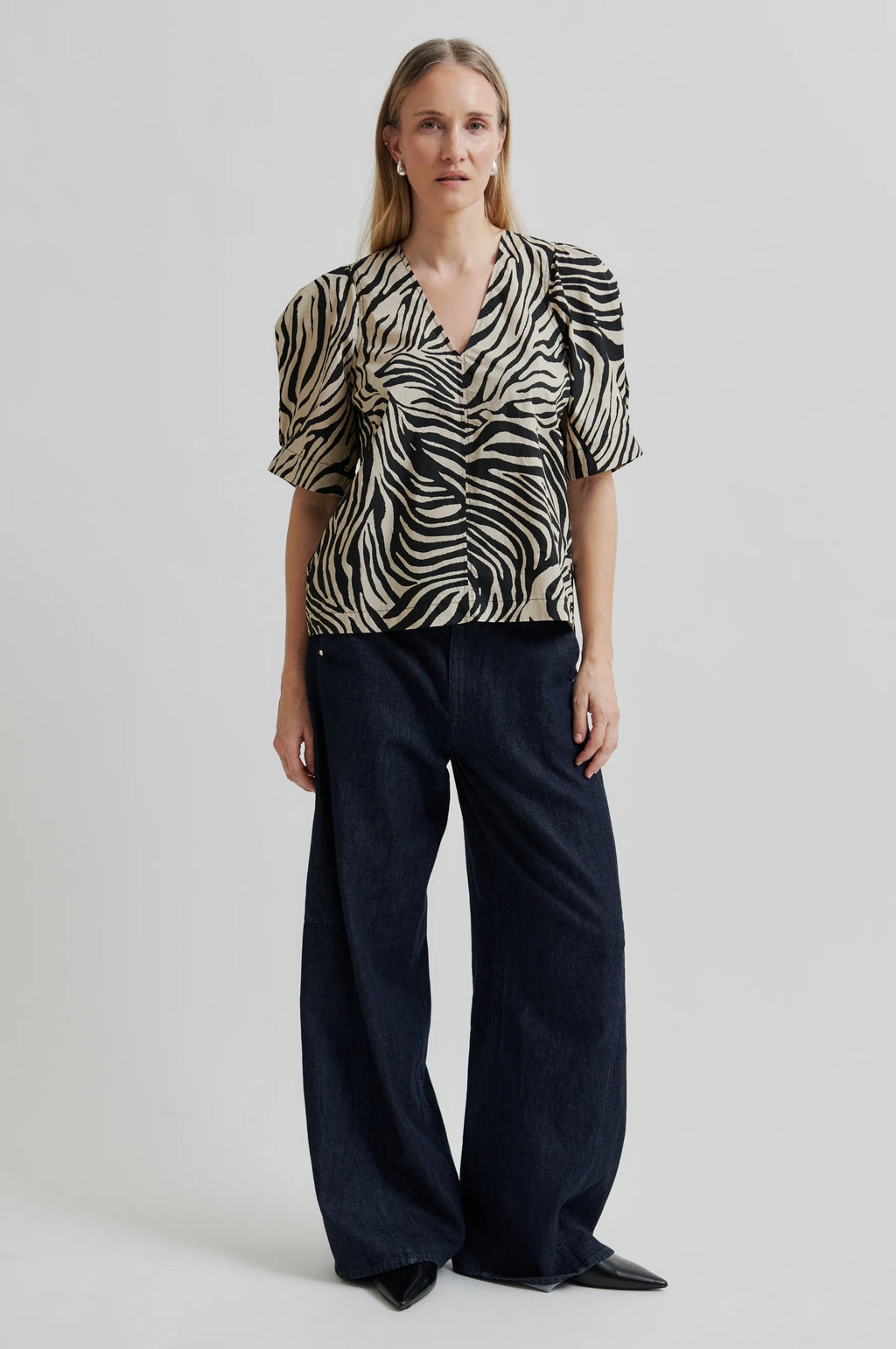 Woman wearing a zebra print top and dark pants on a light background