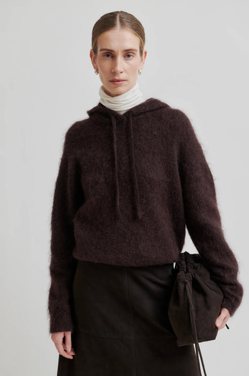 Person wearing a dark brown hoodie and black pants on a light gray background