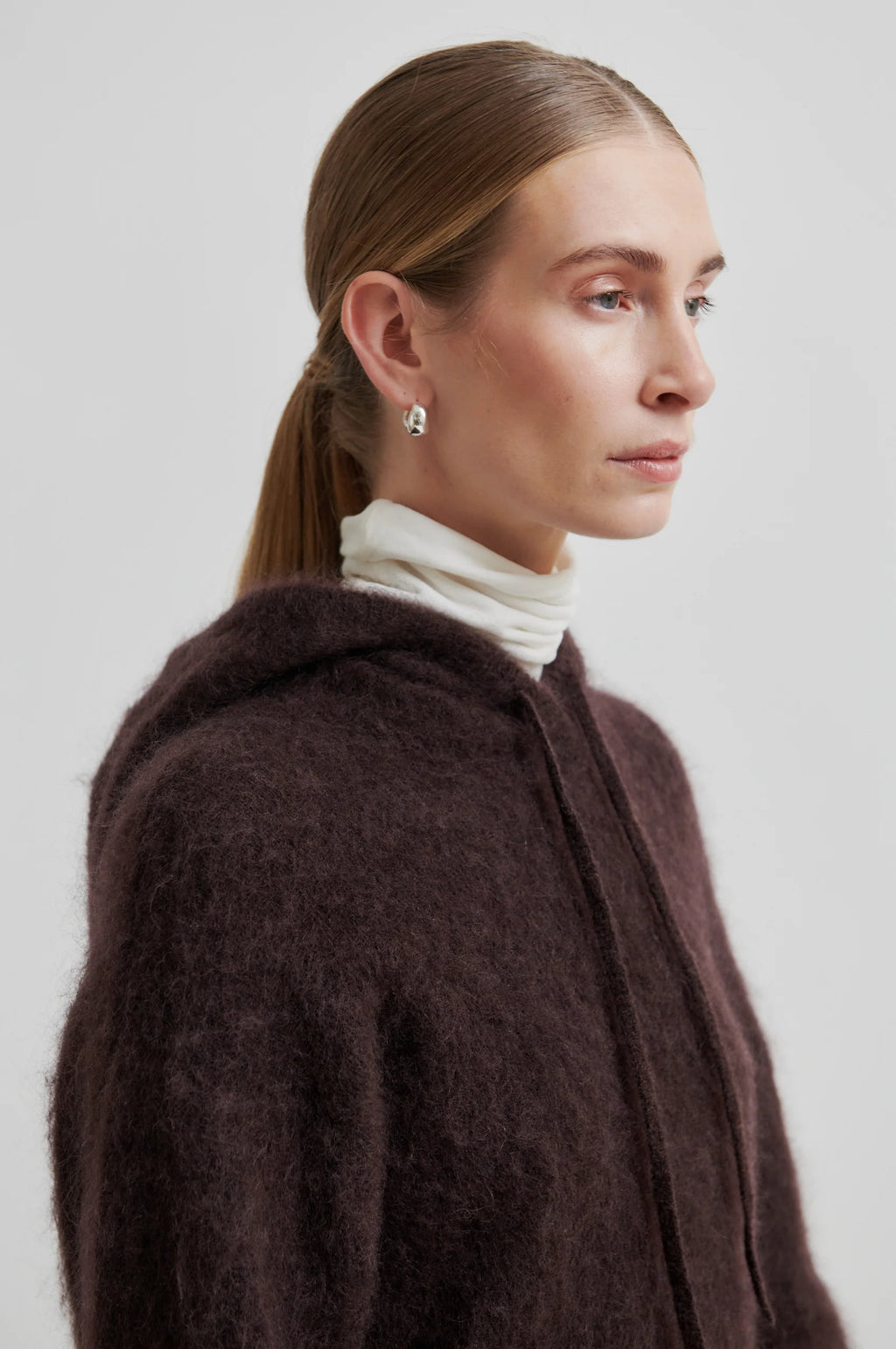 Woman wearing a brown coat over a white turtleneck against a plain background