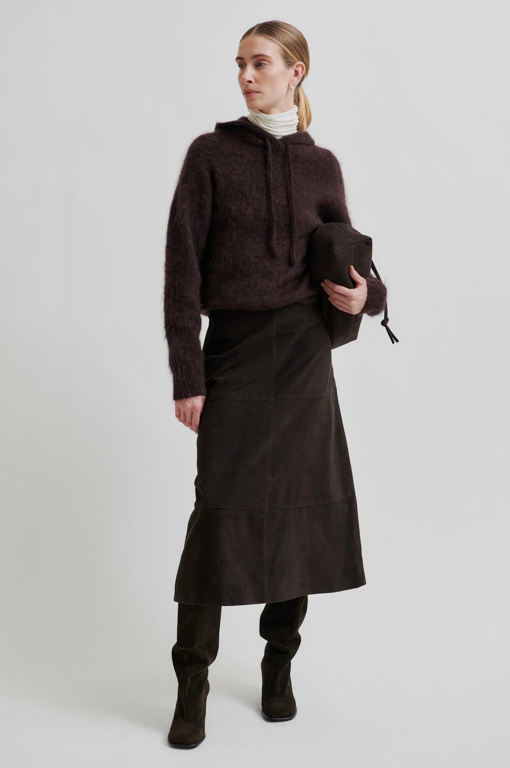 Woman wearing a brown sweater and skirt holding a black bag on a white background