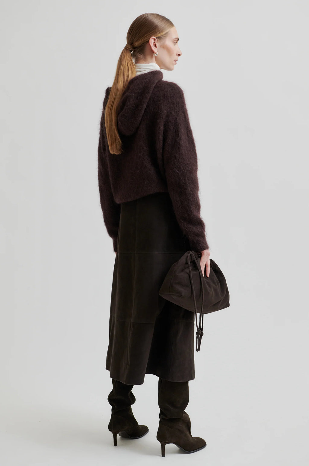 Person wearing a long dark coat with a plain background