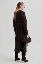 Person wearing a long dark coat with a plain background