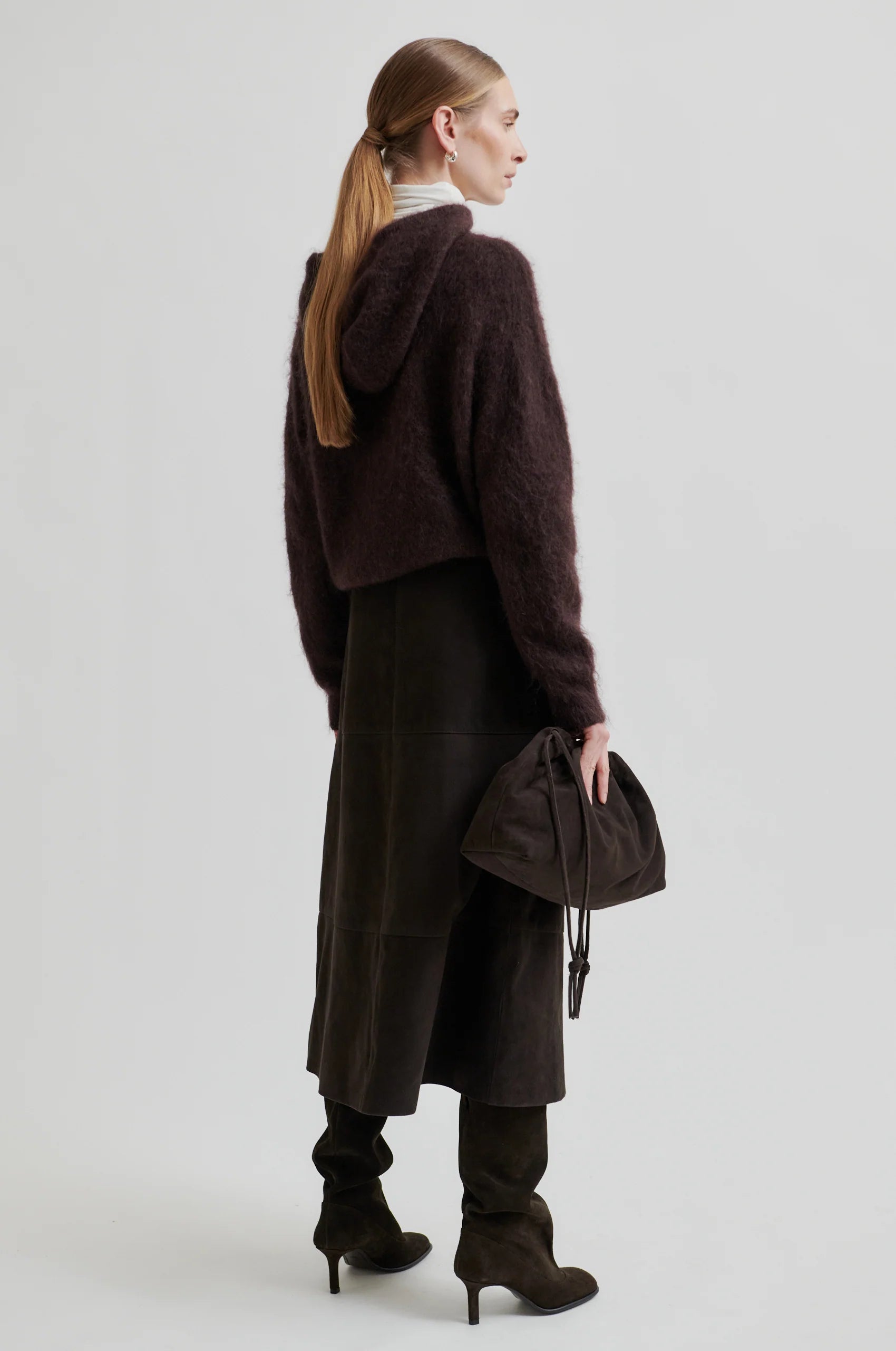 Person wearing a long dark coat with a plain background