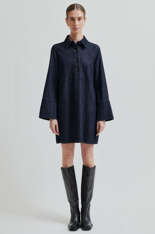 Woman wearing a dark blue dress with long sleeves on a light gray background