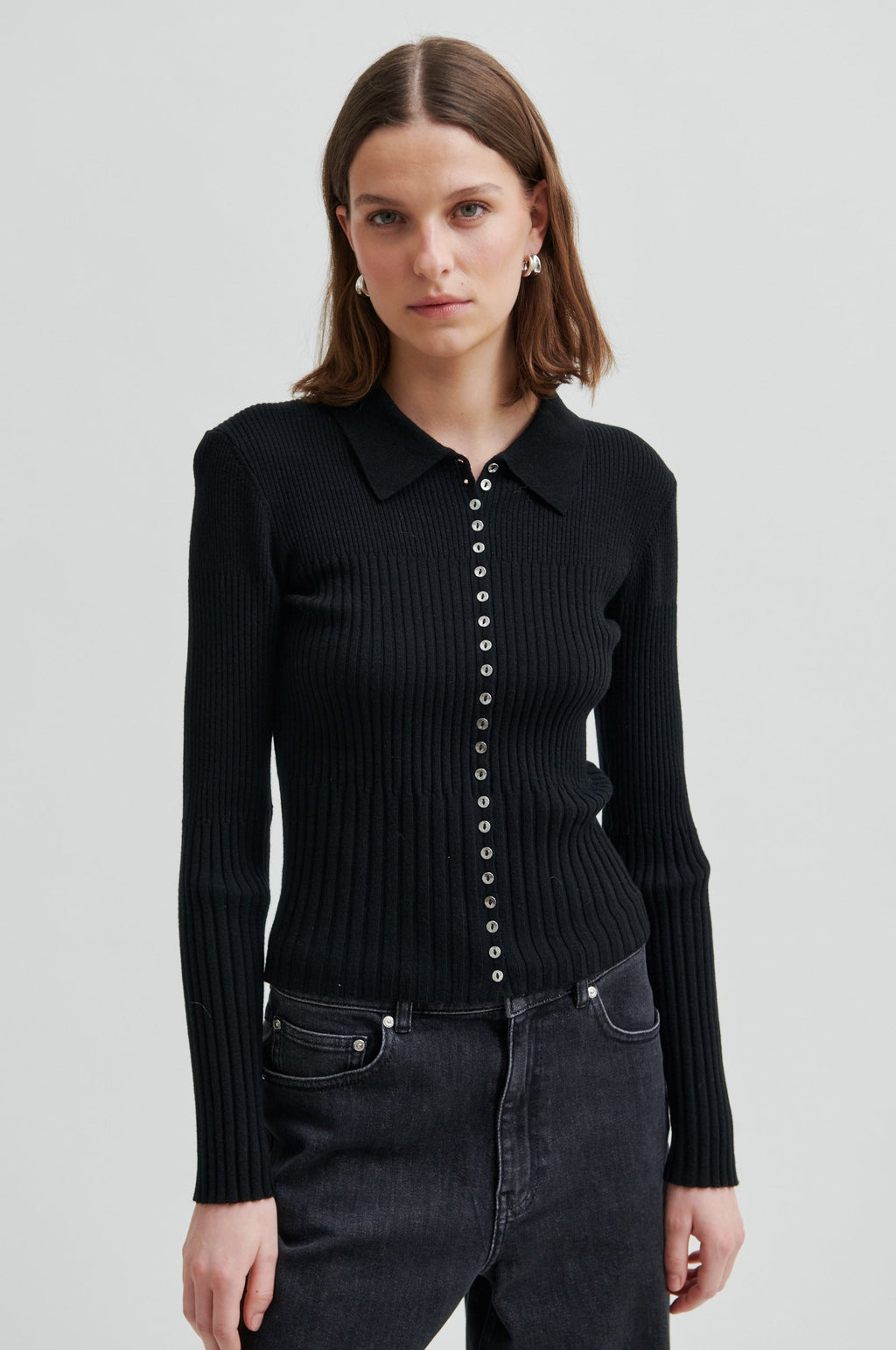 Woman wearing a black ribbed sweater with button details on a light gray background.Jet Knit Cardigan second female 