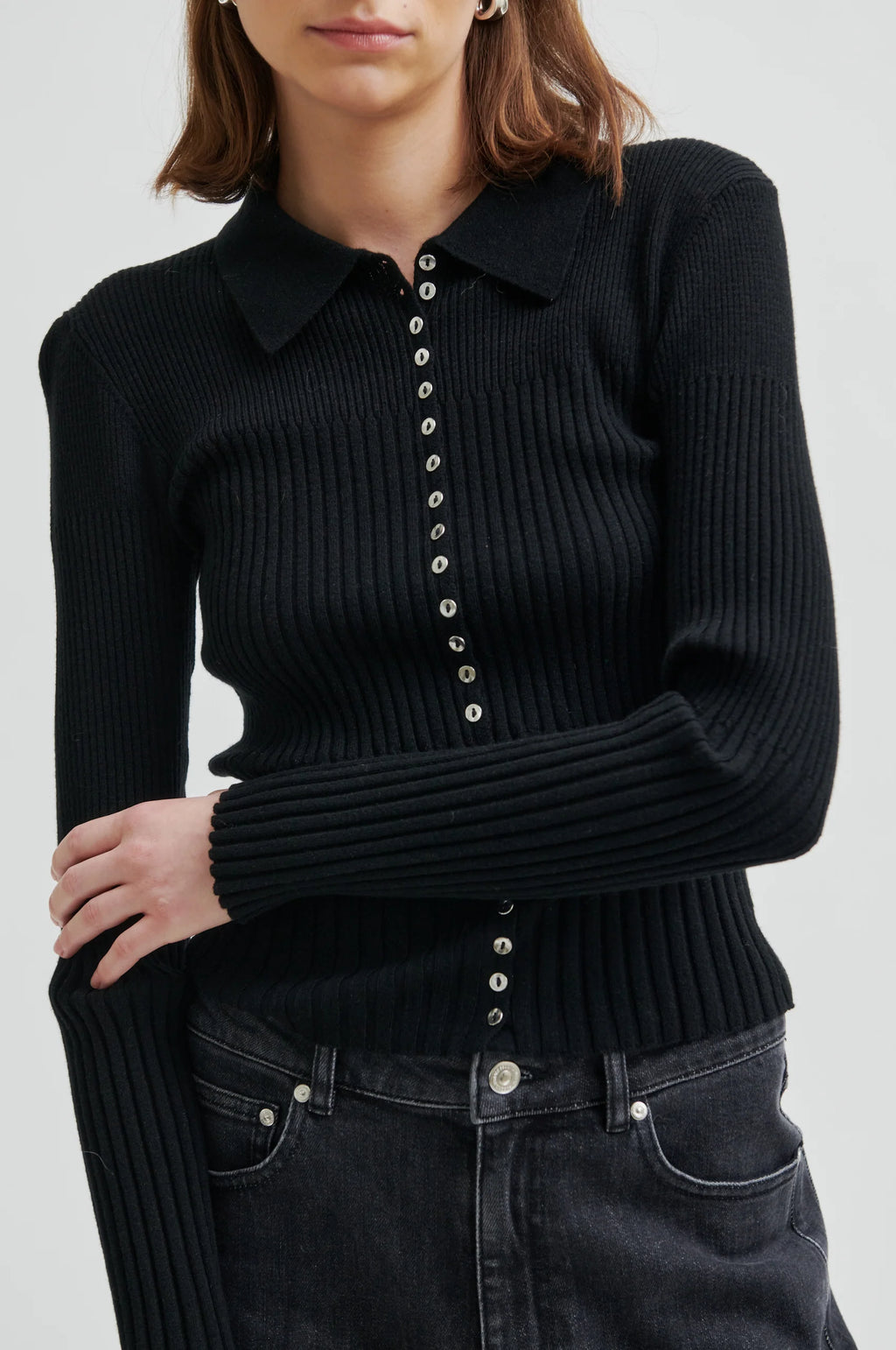 Black ribbed sweater with button details worn by a person on a white background