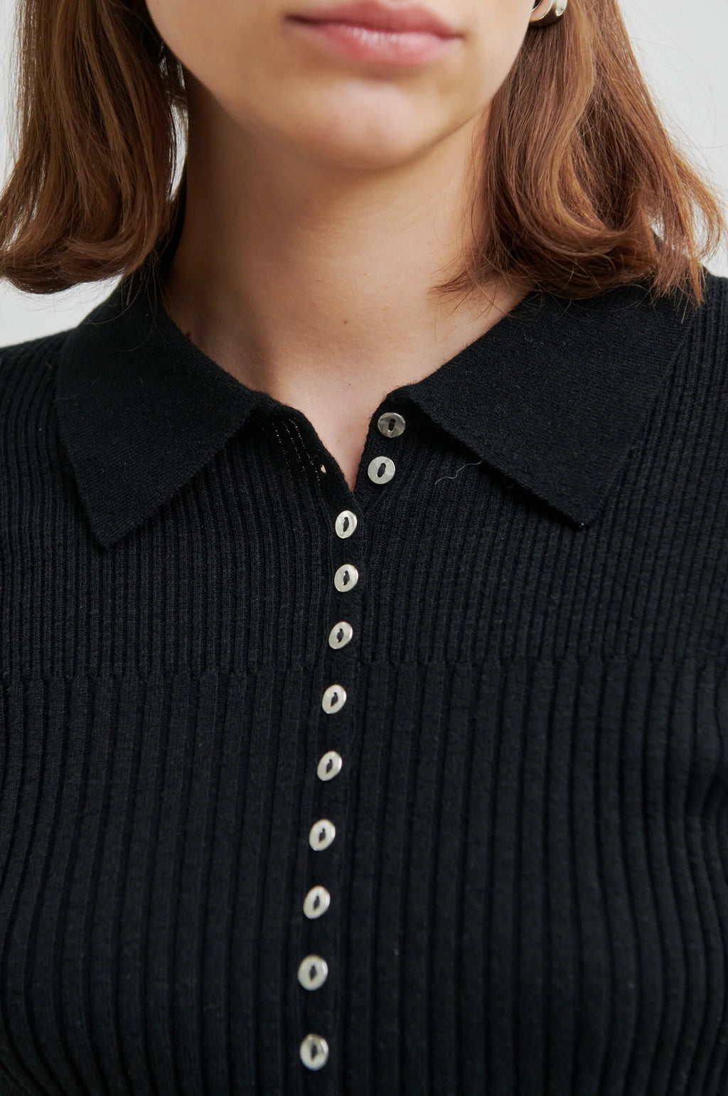 Close-up of a black ribbed sweater with button details on a plain background