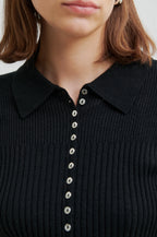 Close-up of a black ribbed sweater with button details on a plain background