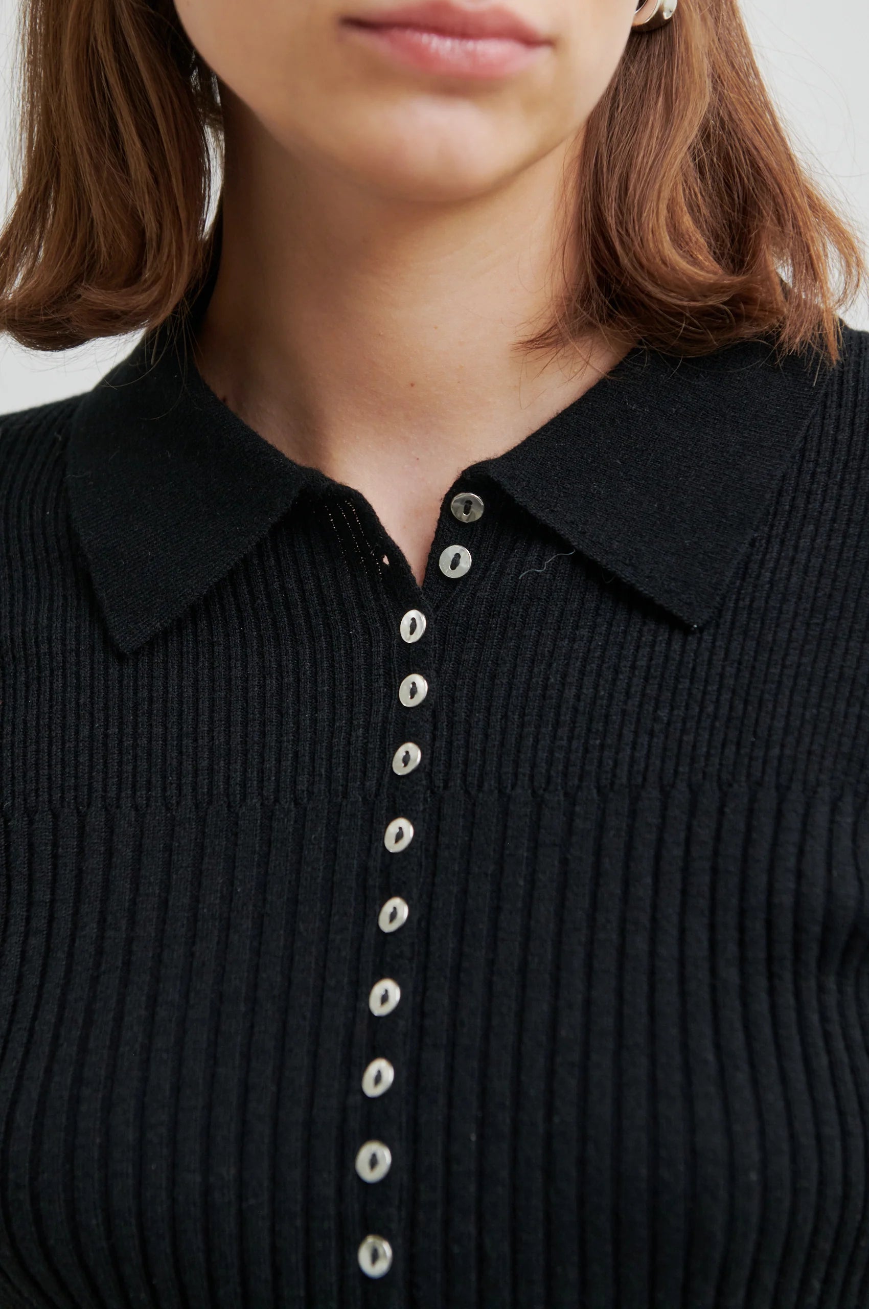 Close-up of a black ribbed sweater with button details on a plain background