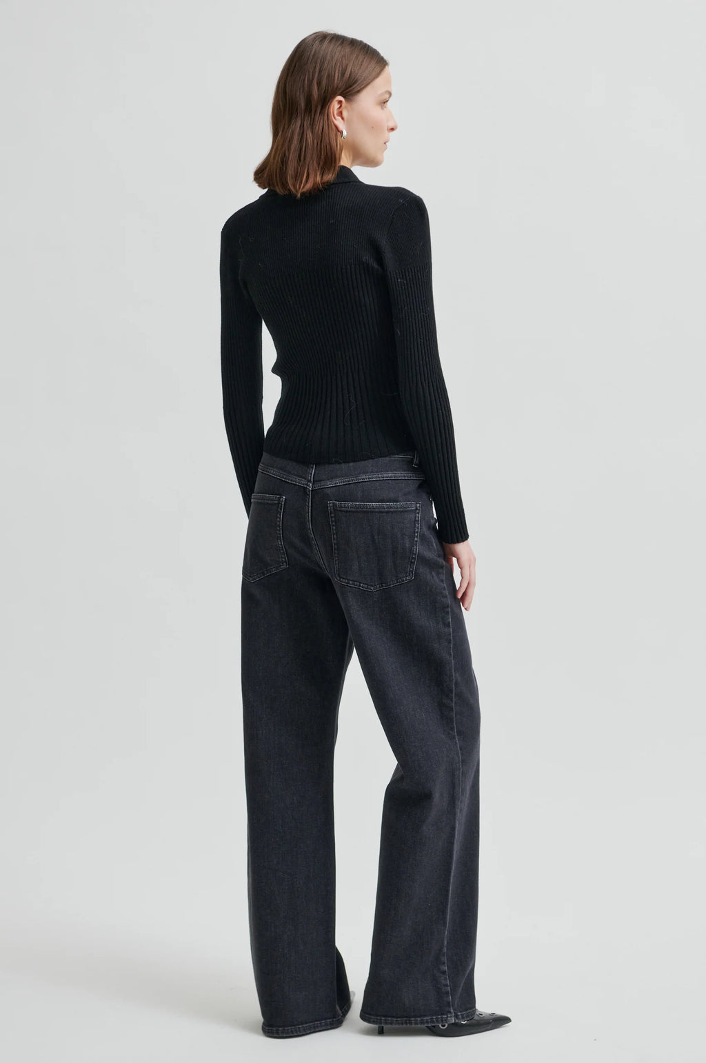 Person wearing a black ribbed sweater and dark jeans on a light gray background