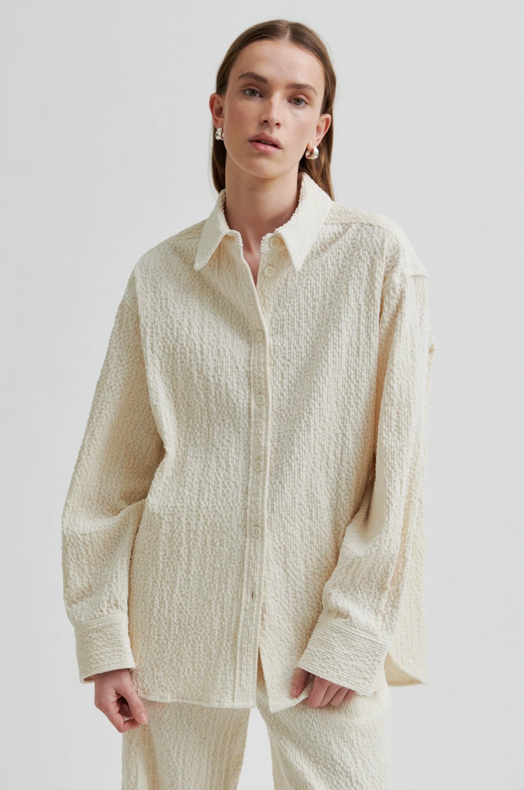 Person wearing a textured beige shirt and pants on a plain background