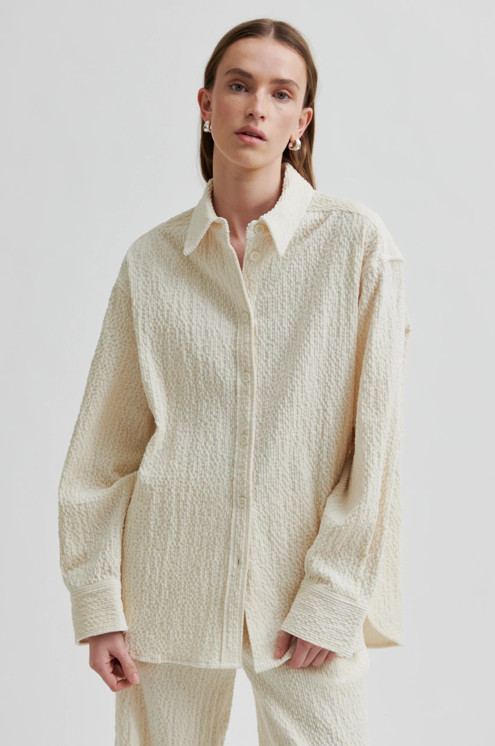 Person wearing a textured beige shirt and pants on a plain background