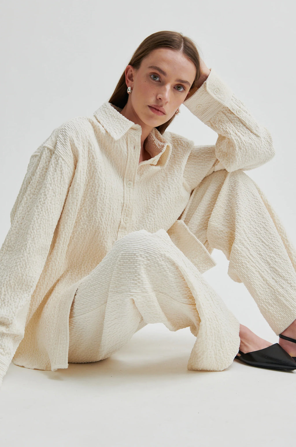 Woman wearing a textured cream outfit sitting on a white background