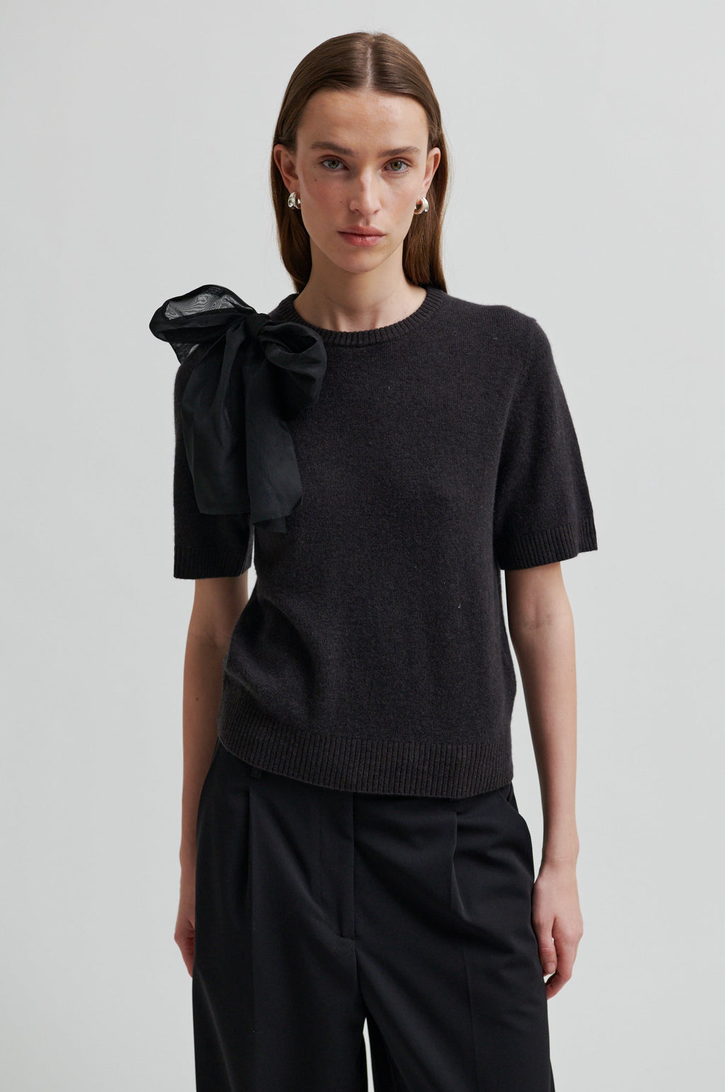 Woman wearing a black top with a bow detail on a plain background.Leara Knit O-Neck second Female 
