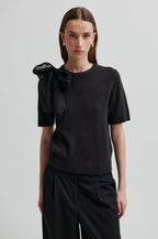 Woman wearing a black top with a bow detail on a plain background.Leara Knit O-Neck second Female 
