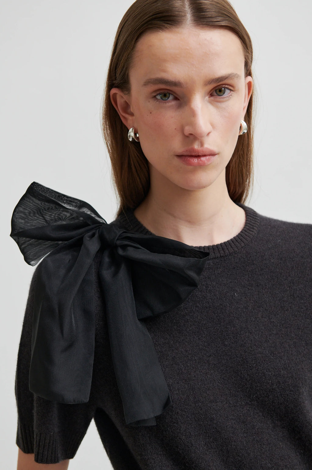 Woman wearing a black sweater with a large bow detail on a plain background