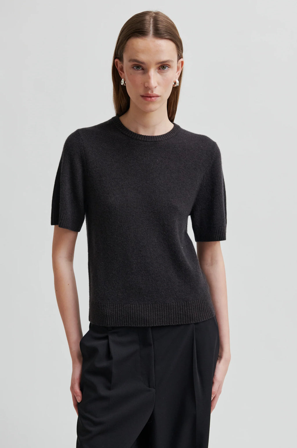 Person wearing a black short-sleeve sweater and black pants on a light gray background