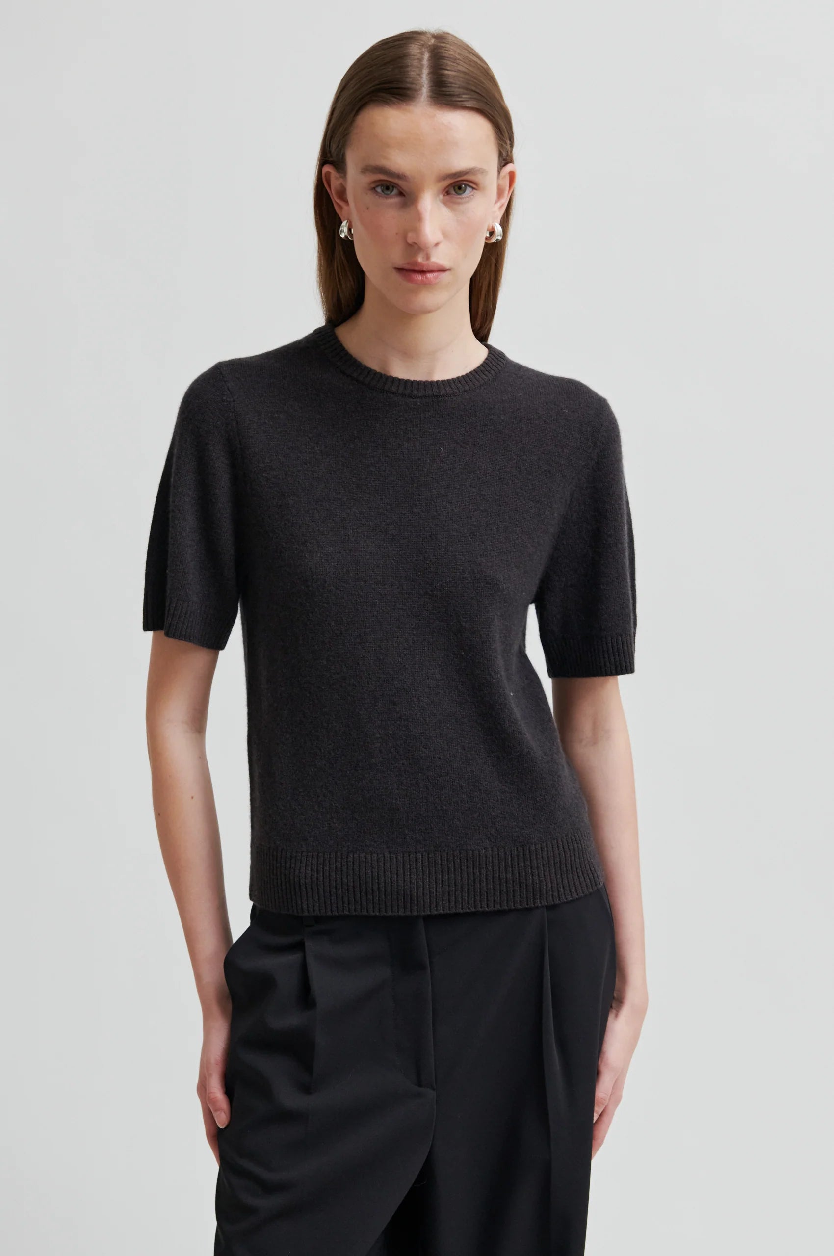 Person wearing a black short-sleeve sweater and black pants on a light gray background
