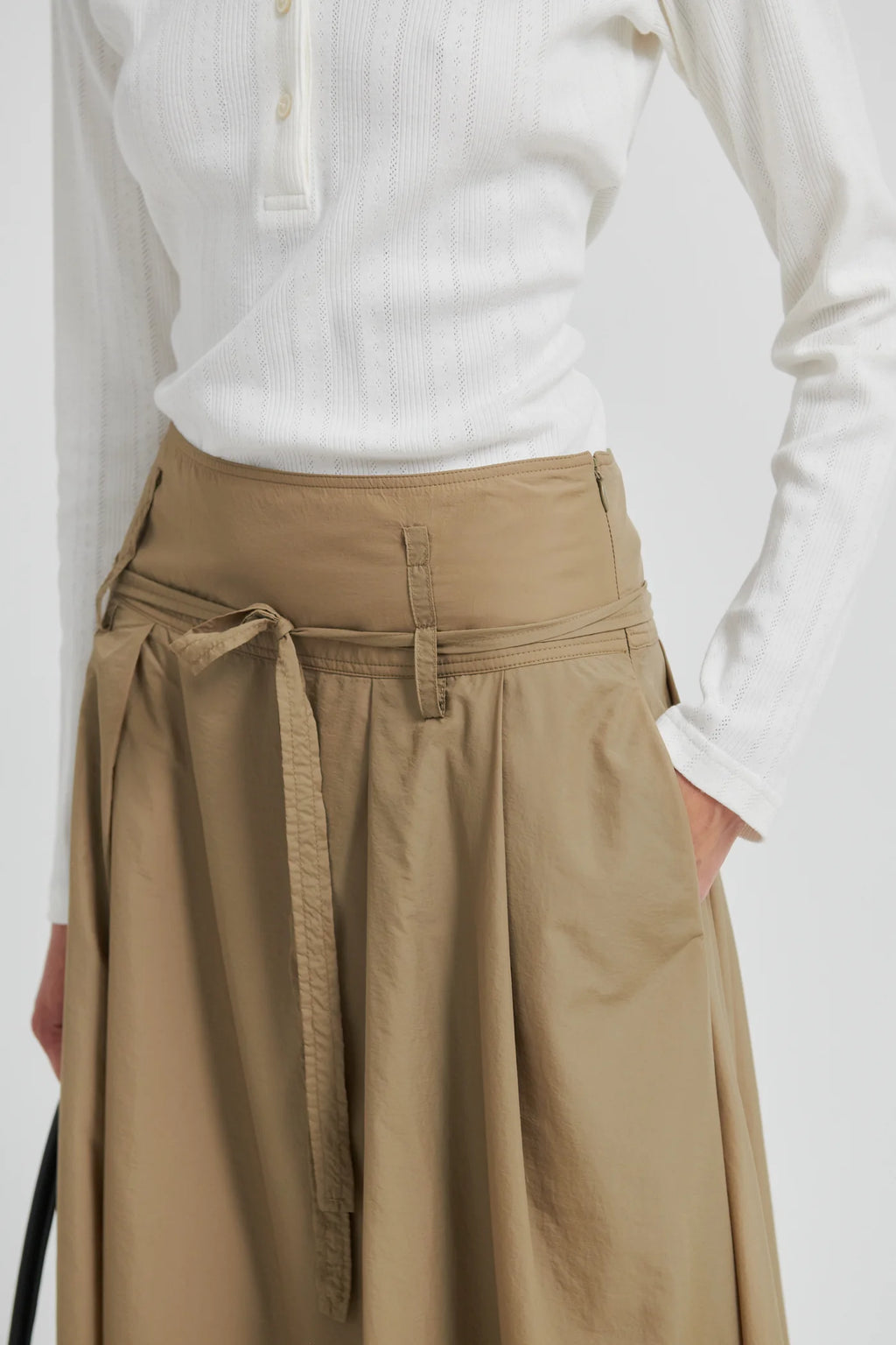 Person wearing a white long-sleeve shirt and beige skirt with a belt on a white background