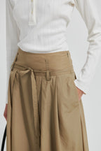 Person wearing a white long-sleeve shirt and beige skirt with a belt on a white background