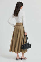 Woman wearing a white blouse and beige skirt, holding a black handbag on a white background