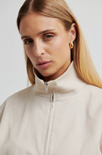 Woman wearing a beige high-neck jacket with a plain background