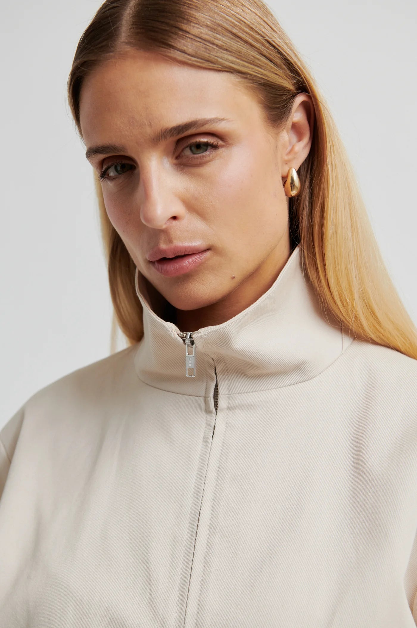 Woman wearing a beige high-neck jacket with a plain background