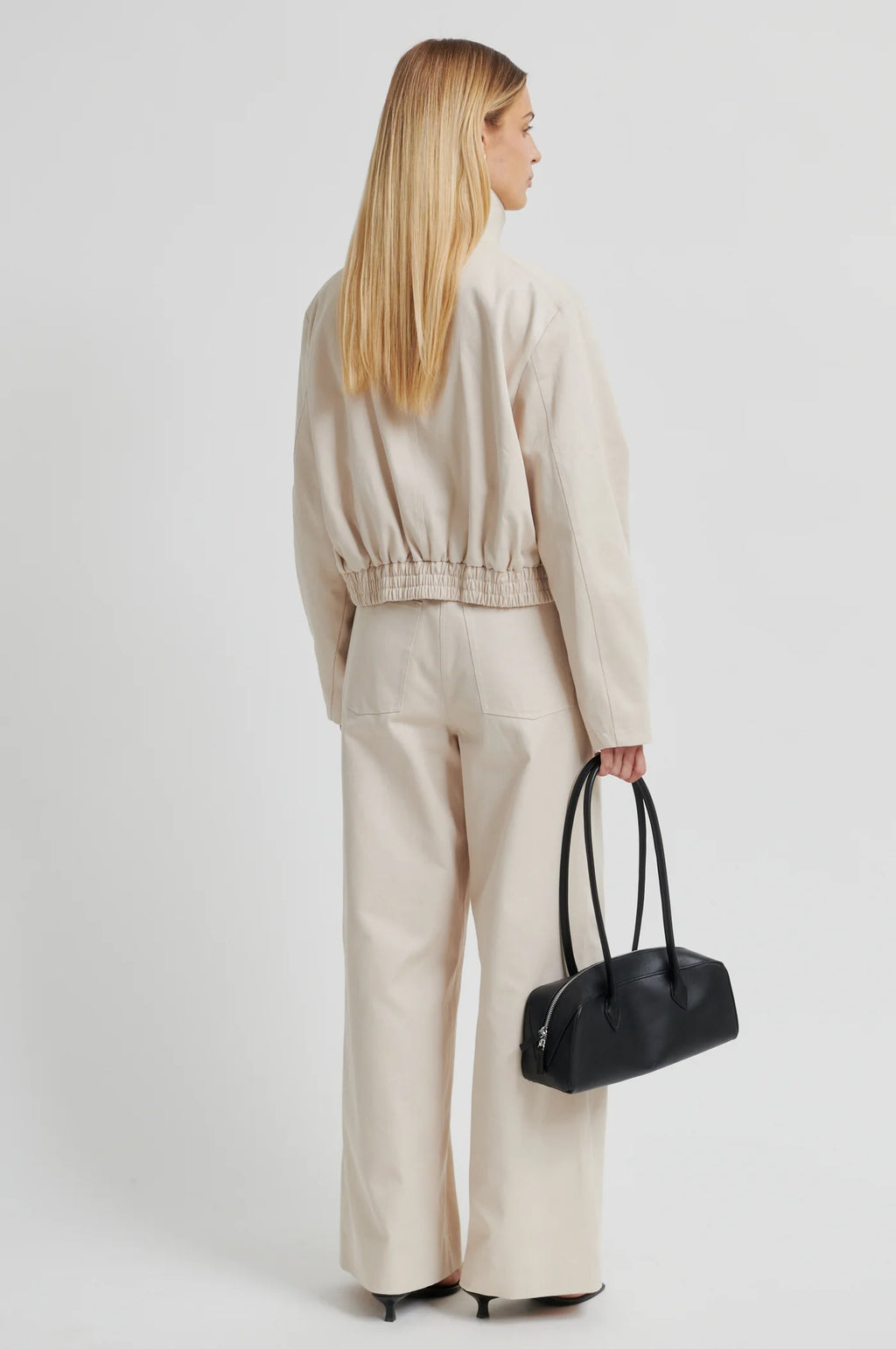 Woman in beige outfit holding a black handbag on a white background