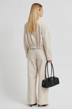 Woman in beige outfit holding a black handbag on a white background