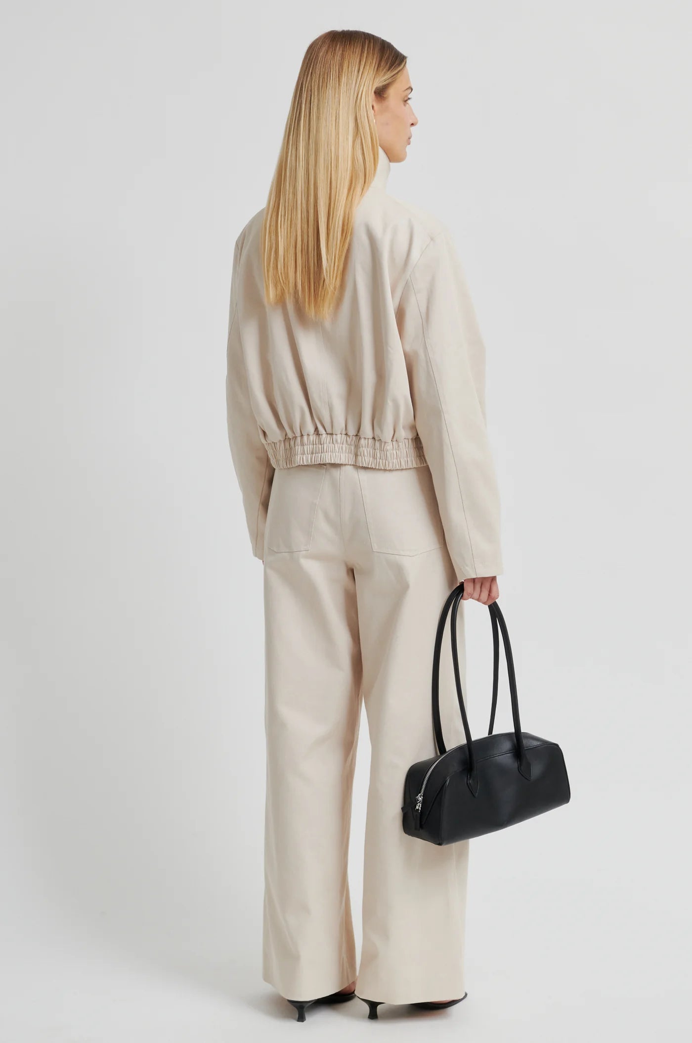 Woman in beige outfit holding a black handbag on a white background