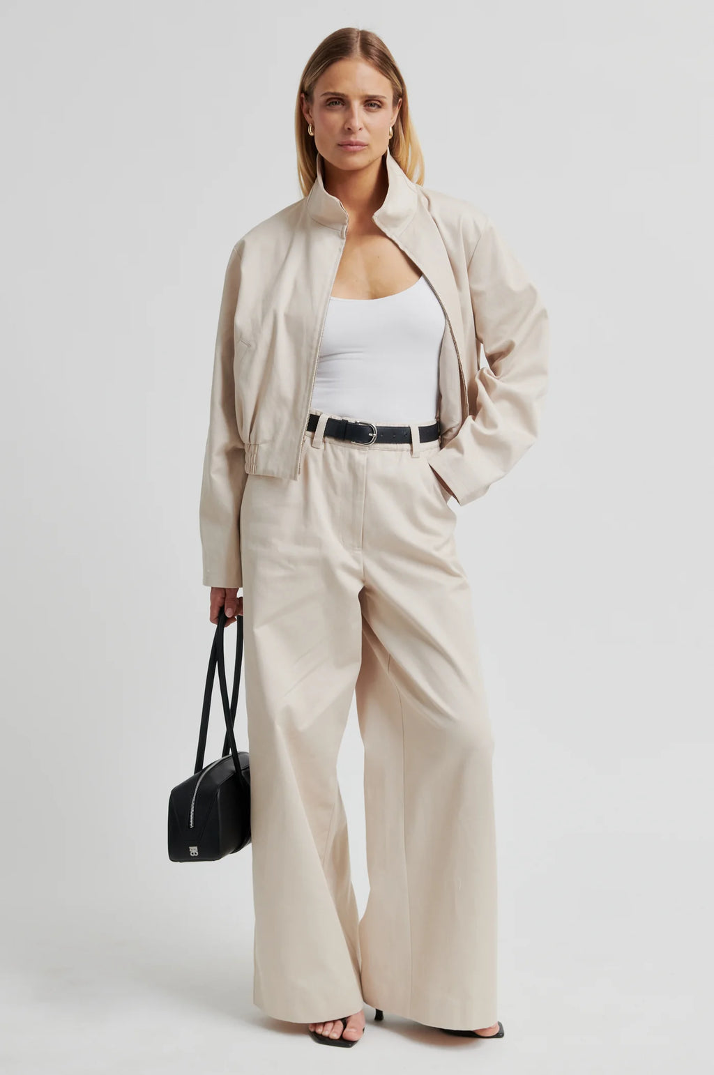 Woman wearing a beige outfit with wide-leg pants and a black bag on a white background