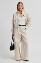Woman wearing a beige outfit with wide-leg pants and a black bag on a white background
