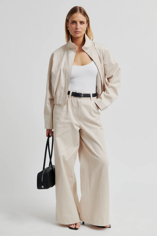 Woman wearing a beige outfit with wide-leg pants and a black bag on a white background
