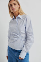 Woman wearing a light blue shirt with a tie-waist design on a white background