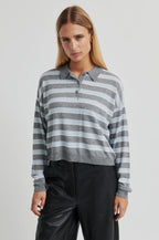Woman wearing a gray and white striped sweater with black pants on a light gray background