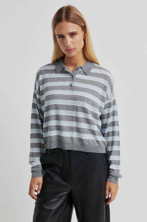 Woman wearing a gray and white striped sweater with black pants on a light gray background