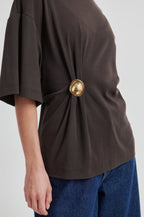 Brown top with a gold button and blue jeans on a white background