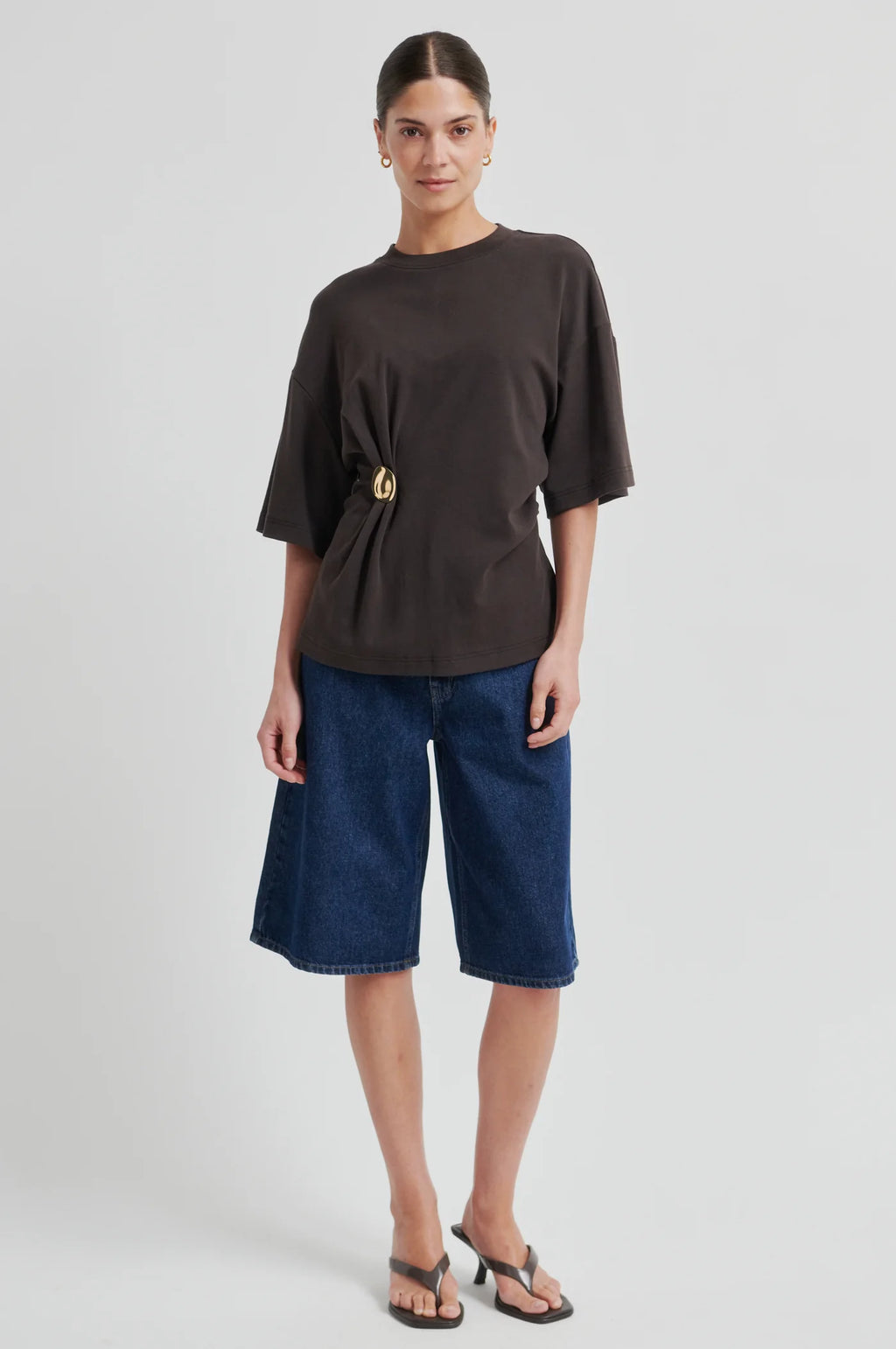 Woman wearing a brown top and blue denim shorts on a light gray background